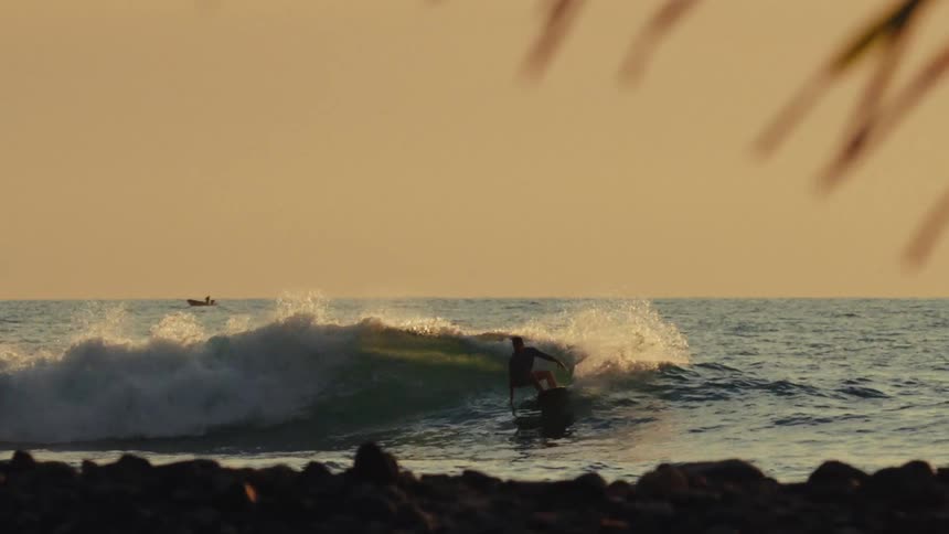 A young man surfs ocean waves close to the beach at sunset