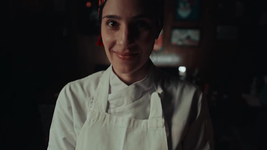 A chef smiles at the camera while holding a plate of food