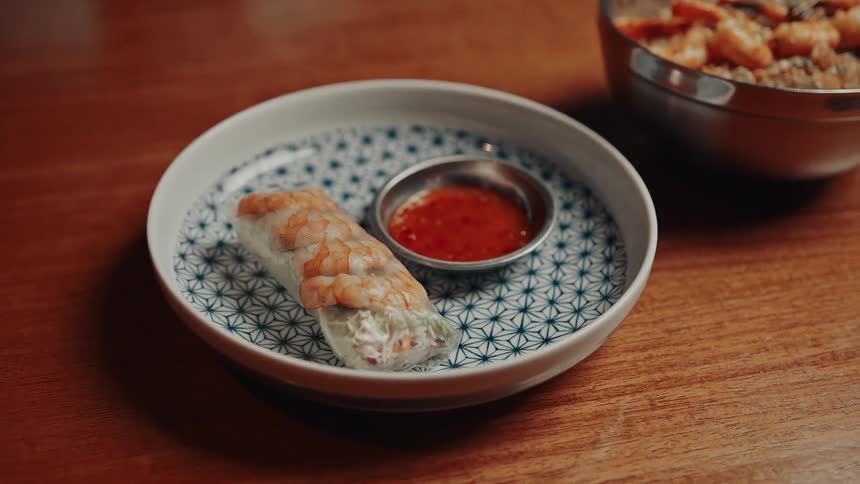 A shrimp spring roll and dipping sauce are plated on a patterned dish