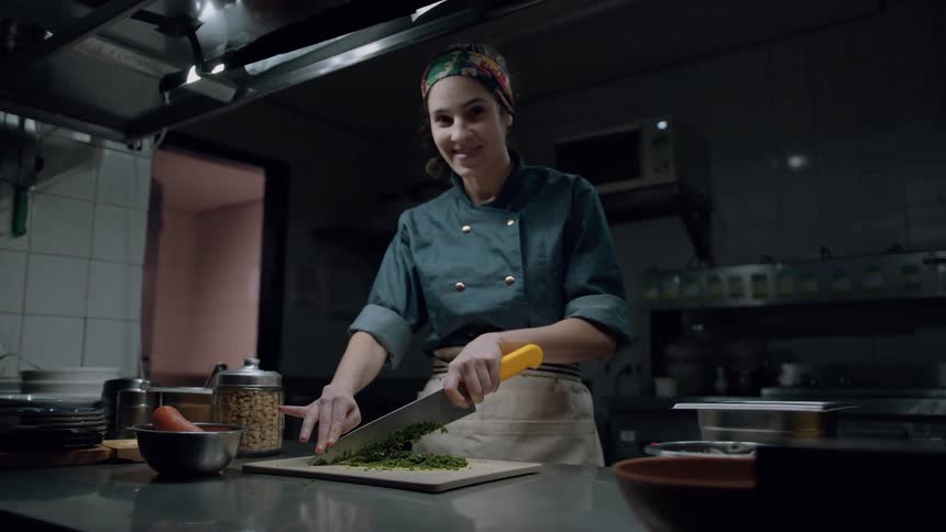 A young female chef chops vegetables on a board with a knife while standing in the kitchen