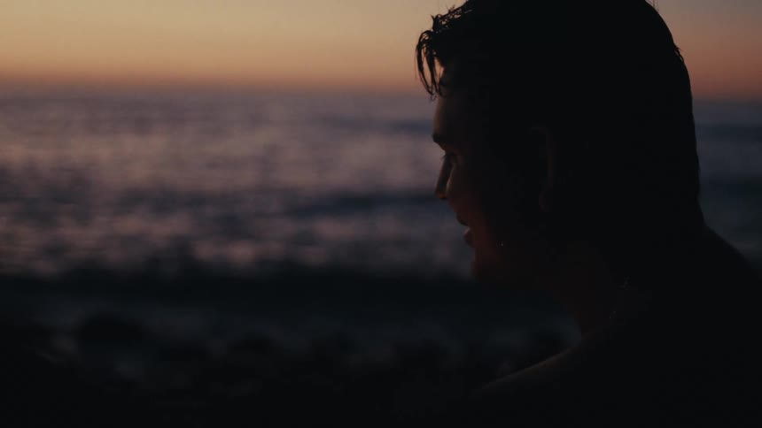 A man stands on the beach at sundown talking to someone else