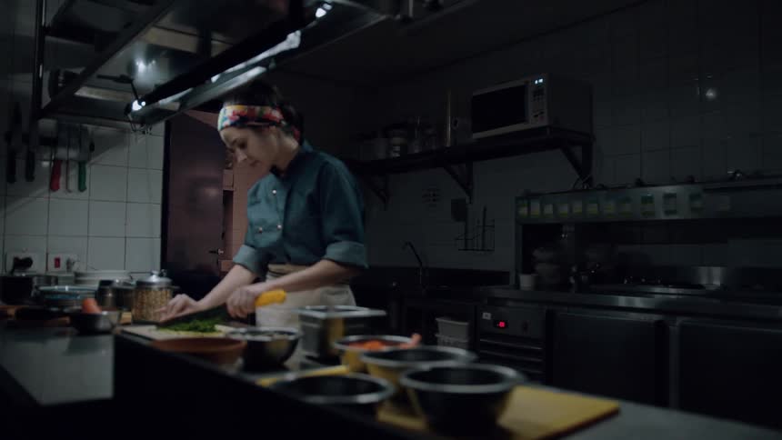 A young female chef cuts vegetables on a chopping board in the kitchen