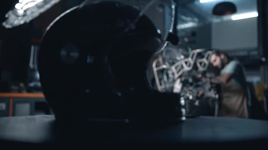 A motorcycle helmet sits on a workbench while a mechanic works on a motorcycle inside a mechanic workshop