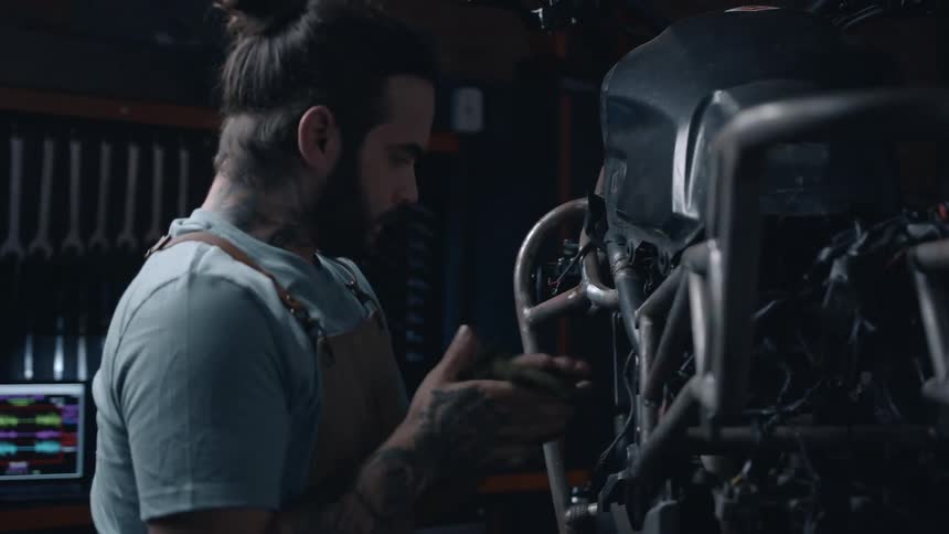A man wipes his hands with a rag while next to a motorcycle in a garage