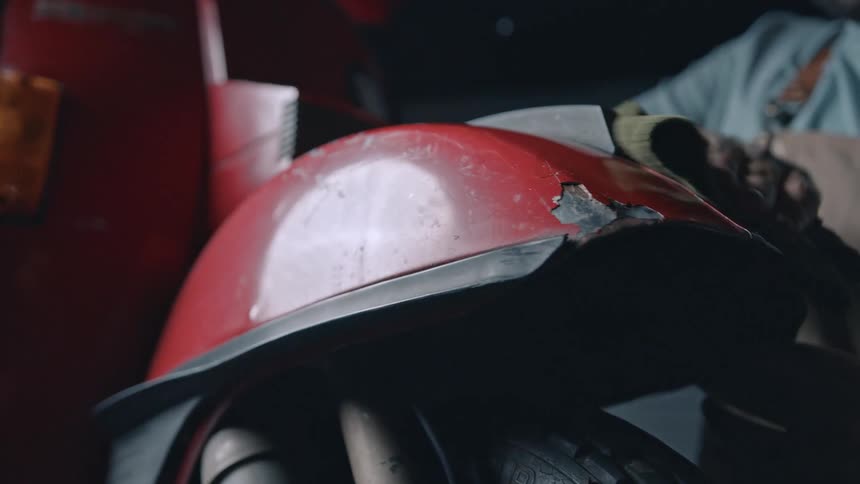 A red motorcycle fender with some damage is wiped clean by a hand holding a green cloth
