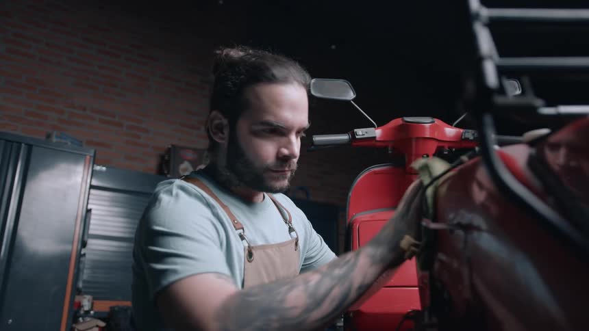 A mechanic cleans a red motorcycle with a cloth in a repair shop