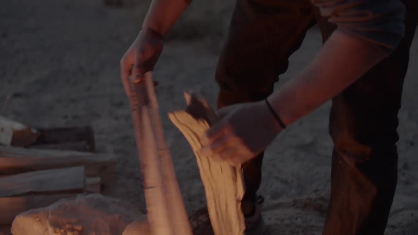 Man carries kindling to a lit campfire
