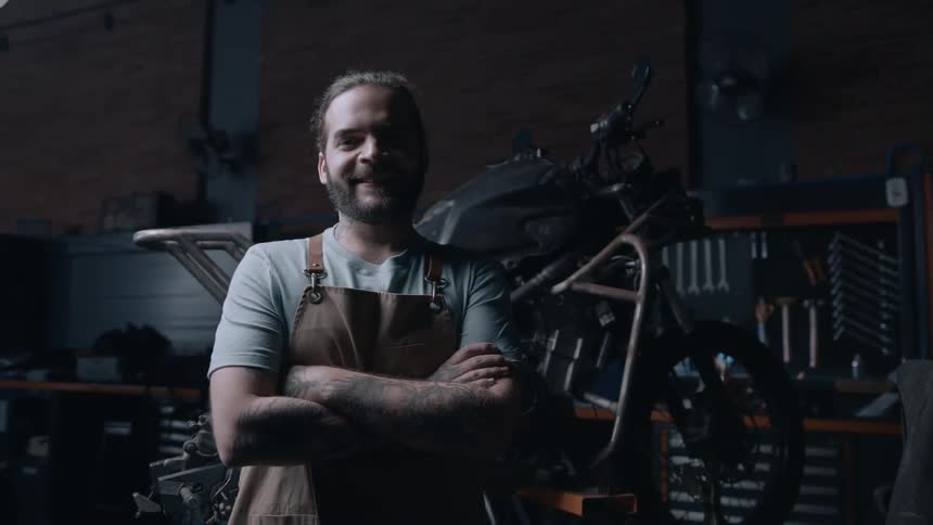 A man standing with his arms crossed in a motorcycle workshop smiling
