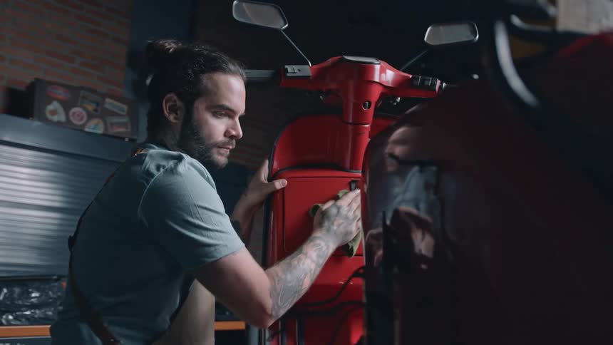 Man cleans the front of a red scooter with a green cloth