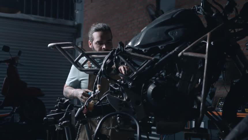 A mechanic works intently on a strippeddown motorcycle frame in a dimly lit garage