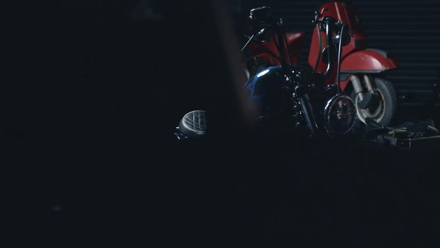 A custom motorcycle with blue flames sits beside a red scooter in a dim garage
