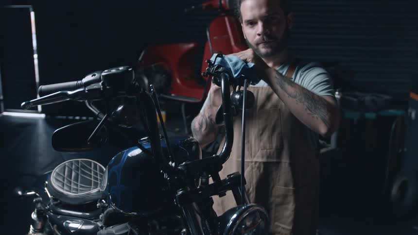 A focused mechanic works on cleaning a motorcycle in a dimly lit garage