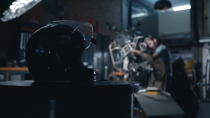 A technician fixes a motorcycle inside a mechanic workshop with a crash helmet on a table next to him