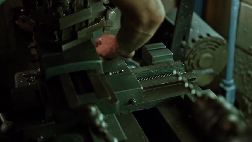 A hand cleans parts of a lathe machine with a brush in a workshop