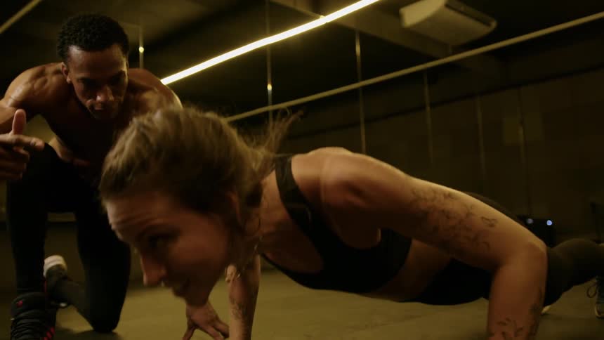 A trainer motivates a determined woman midpushup during a highintensity workout
