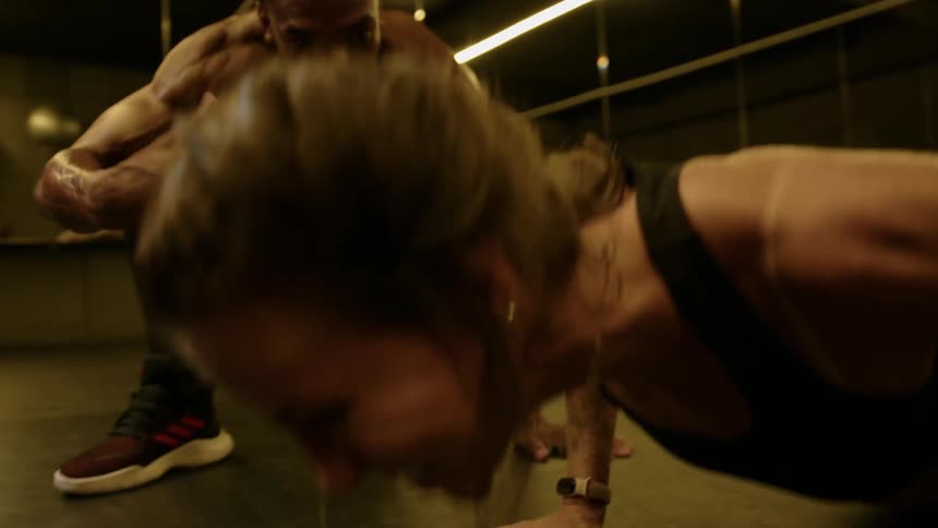 A man encourages a woman who is struggling with pushups in the gym