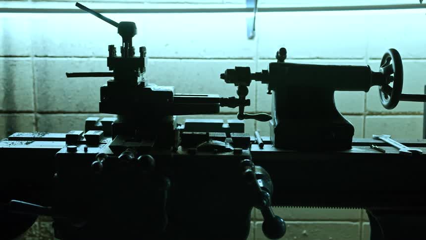 Silhouetted lathe machines sit beneath a glowing overhead light in a dim workshop