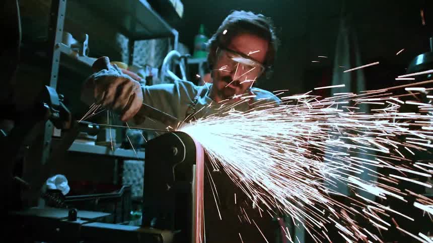 Man with safety glasses and headphones scraping a metal object on a machine with sparks flying