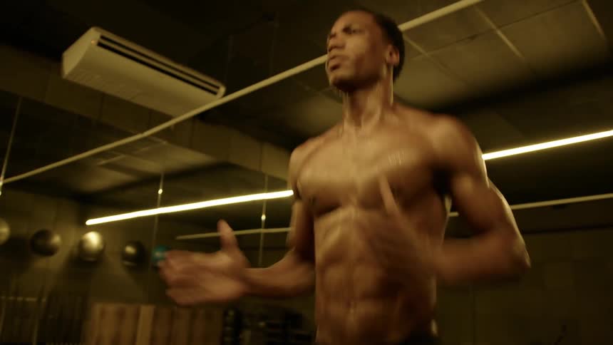 A shirtless young man continues jogging in place in the gym