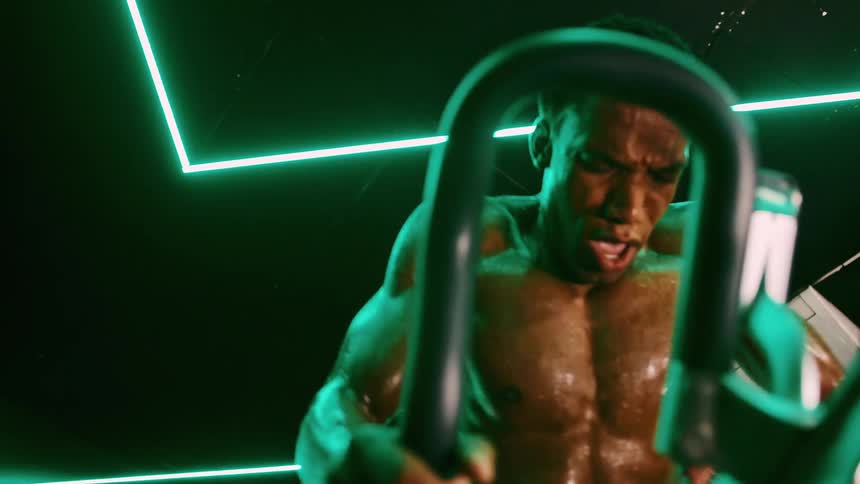 Muscular shirtless and sweaty man performs intense workout on a stationary bike