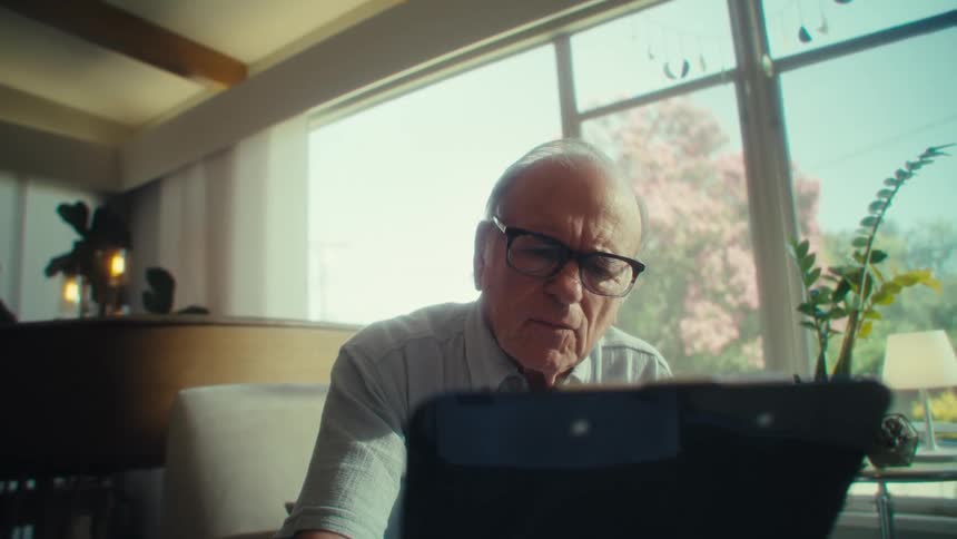 An elderly man reads a paper document on a clipboard while sitting in a room during daytime
