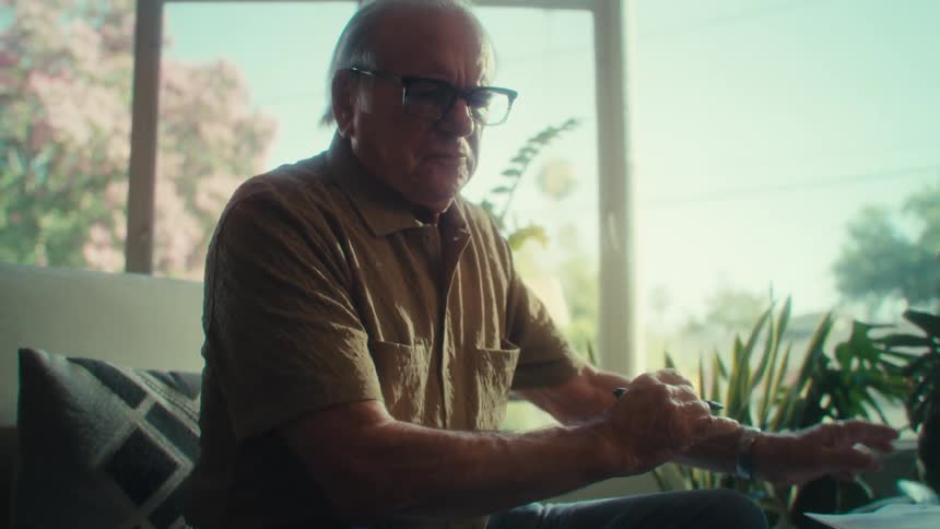 Elderly man sitting analyzing documents papers facing a table with an open laptop