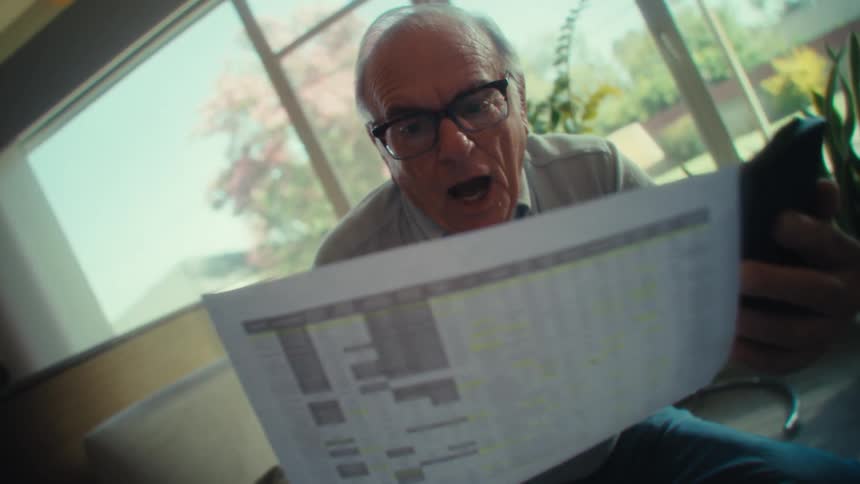 An elderly man celebrates after checking calculations in a paper document with a calculator in a room during daytime