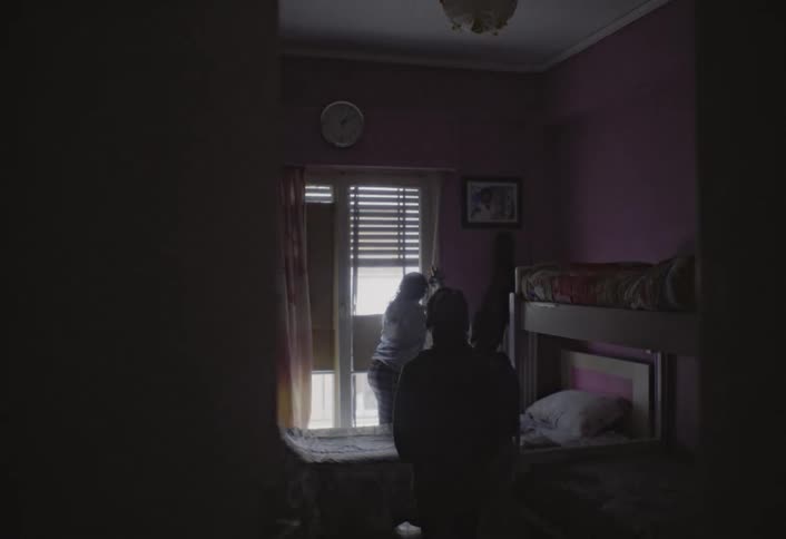 Three children inside a room with a girl opening the window curtain