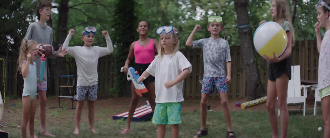 Children with toys jumping and cheering in a backyard