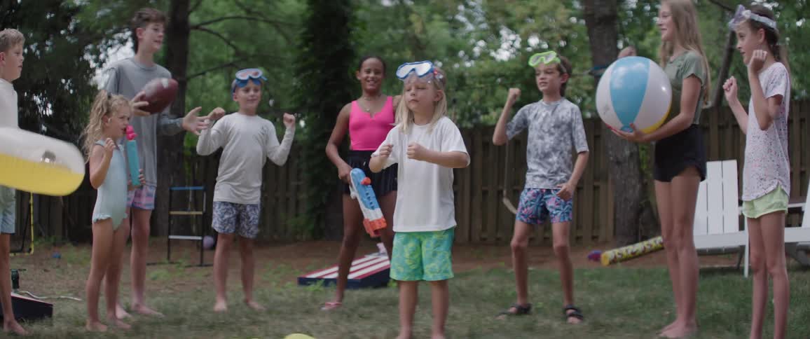 A group of children pump their fists and cheer on a friend at backyard gathering