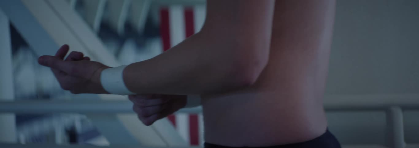 The video opens with a view of a dimly lit room with a window revealing a blurred outdoor scene a woman with long light brown hair then comes into focus appearing thoughtful or contemplative as she looks offcamera to her left