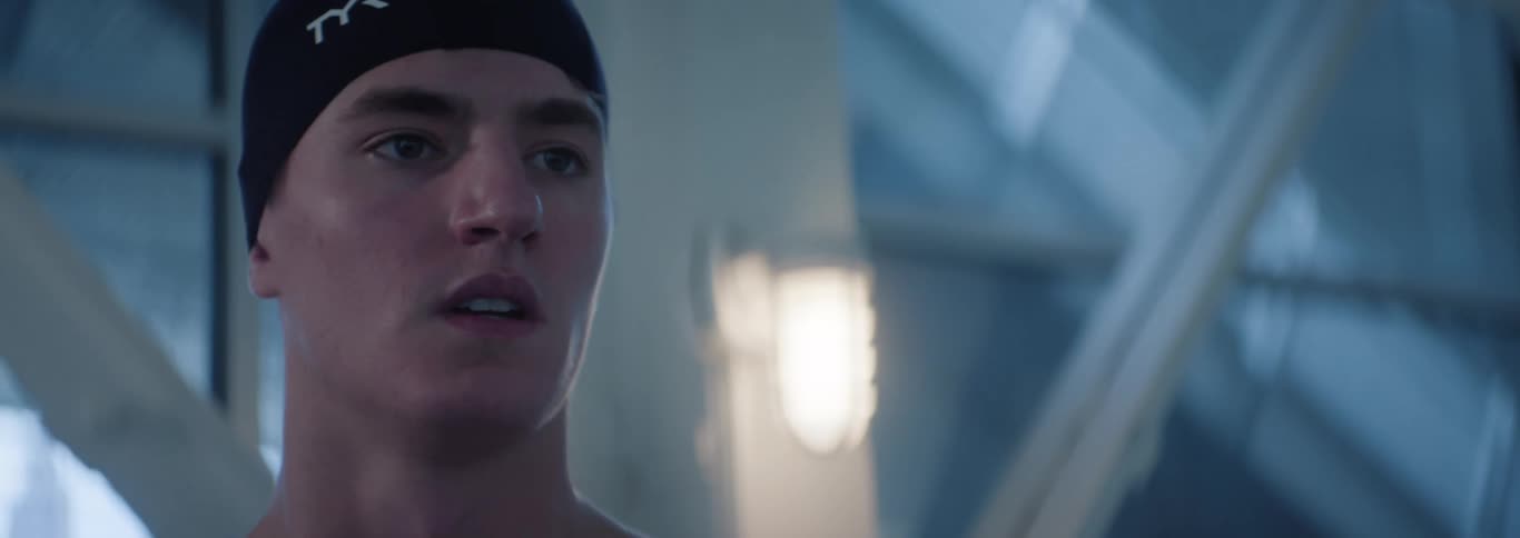 The video features a closeup of a male swimmer wearing a black swim cap he is looking intently to his left appearing focused and ready