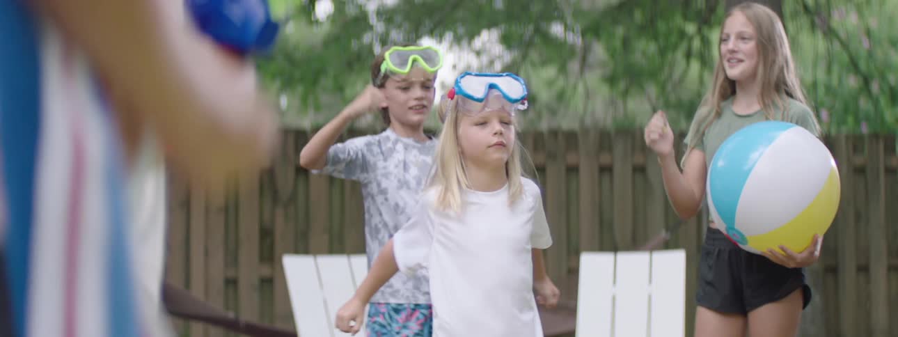 Little blonde girl warming up while other kids around cheer and watch her in a backyard