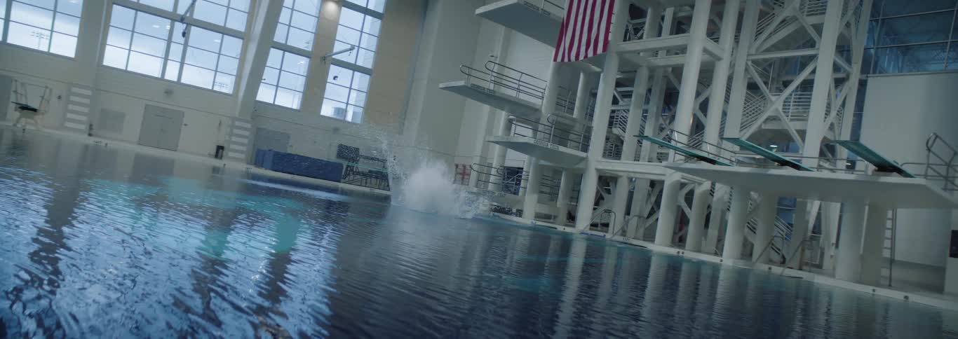 A diver jumps off a diving platform into a large swimming pool at midday during a practice session