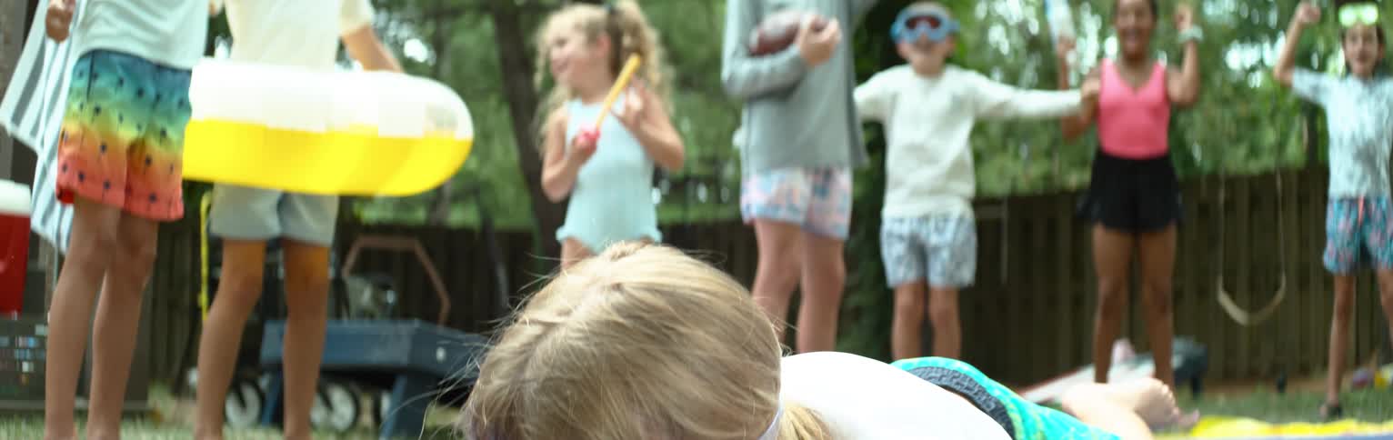 Child lying on the ground on a tarp and other children in the background jumping in a yard