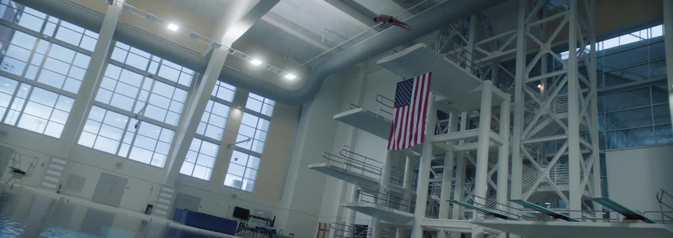 A woman dives off a high platform diving board into an indoor pool