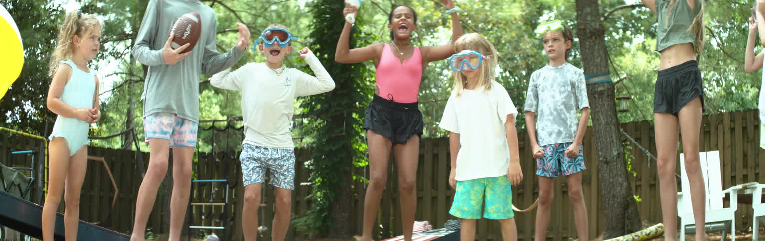 A group of kids jump and cheer for another one about to use a slipandslide