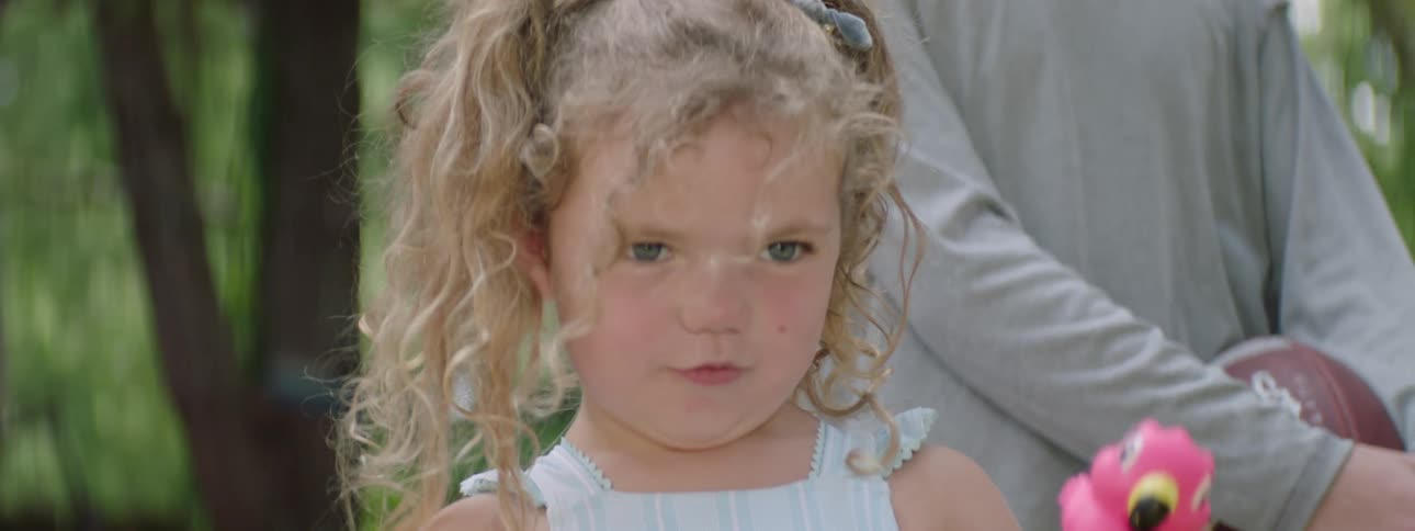 Little blonde girl in a backyard screaming and holding an object and a person next to her