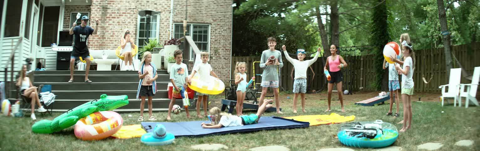 A group of children celebrate after a boy dives to the floor while playing in a backyard during daytime