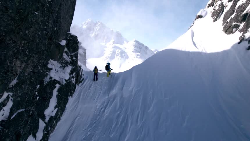 The video features two individuals dressed in winter gear complete with backpacks and ski poles as they ascend a snowcovered mountain the sky above is bright with some scattered clouds suggesting a clear but cold day
