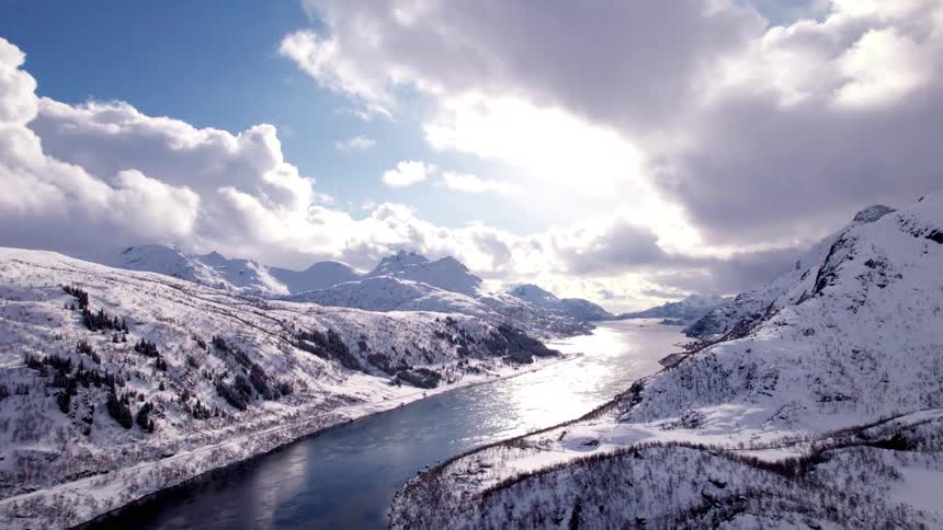 A stream flows through a mountain path in winter with the surrounding mountains covered in icy snow at midday