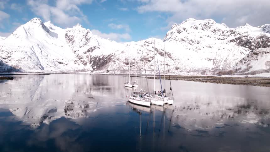 A sailboat is on a lake surrounded by snowcovered mountains in winter at midday