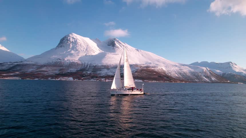 The video features a stunning view of a white sailboat moving across a calm dark blue body of water in the background majestic snowcovered mountains rise under a bright clear sky