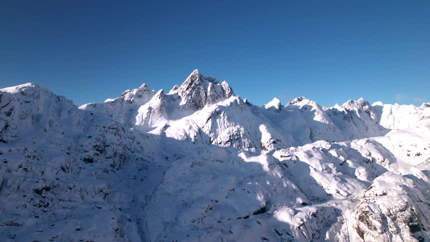 A mountain with a rugged peak is covered in snow during winter at midday
