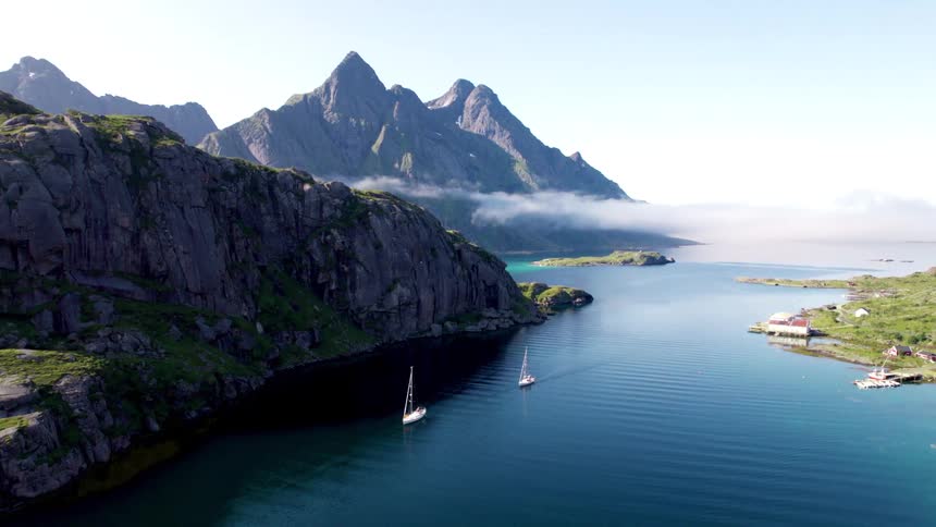 Two small sailboats are anchored by the mountains