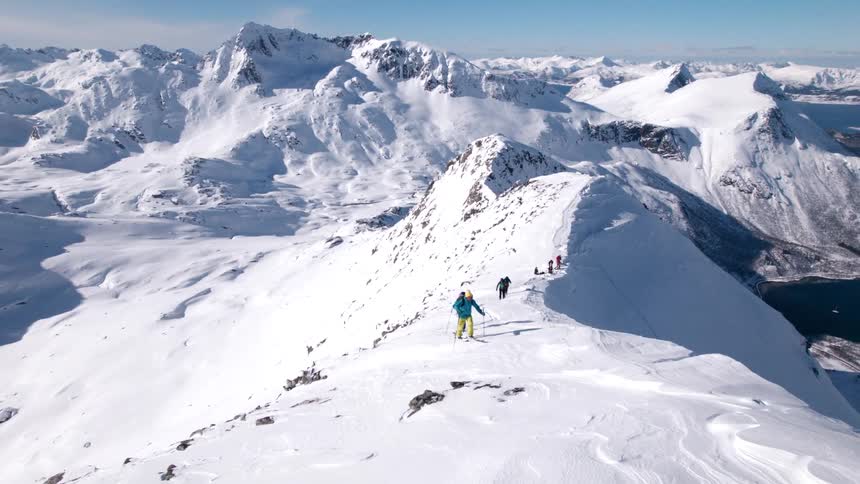 People are hiking up the snow covered mountain on skis by the river