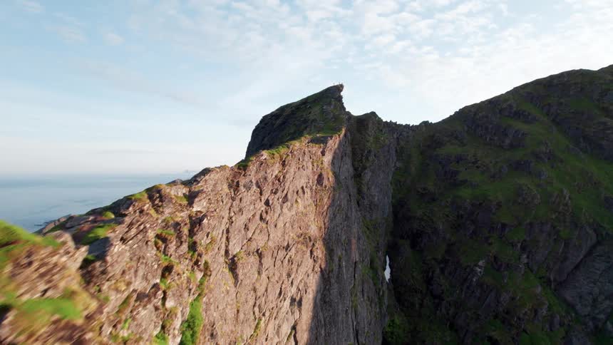 A rugged grassy mountain ridge dotted with rocks rises sharply under a partly cloudy sky