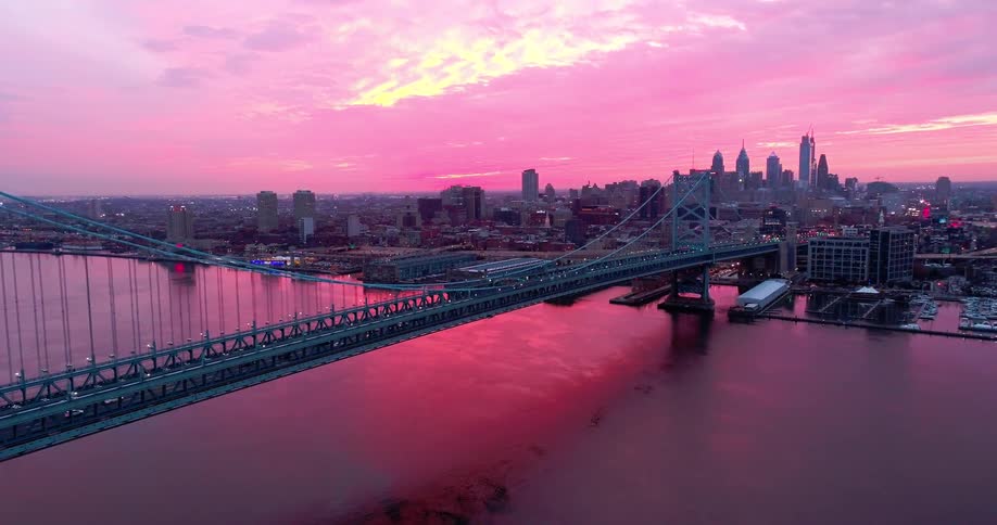 Aerial view of a bridge over the sea with a metropolis in the background on a purple sky sunrise