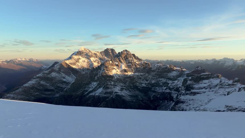 Golden sunlight illuminates a rugged snowdusted mountain range viewed from a high snowy plateau under a clear morning sky