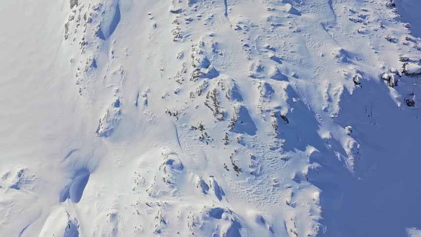 Snowcovered mountain terrain displays sharp ridges scattered rocks and windsculpted drifts under bright daylight